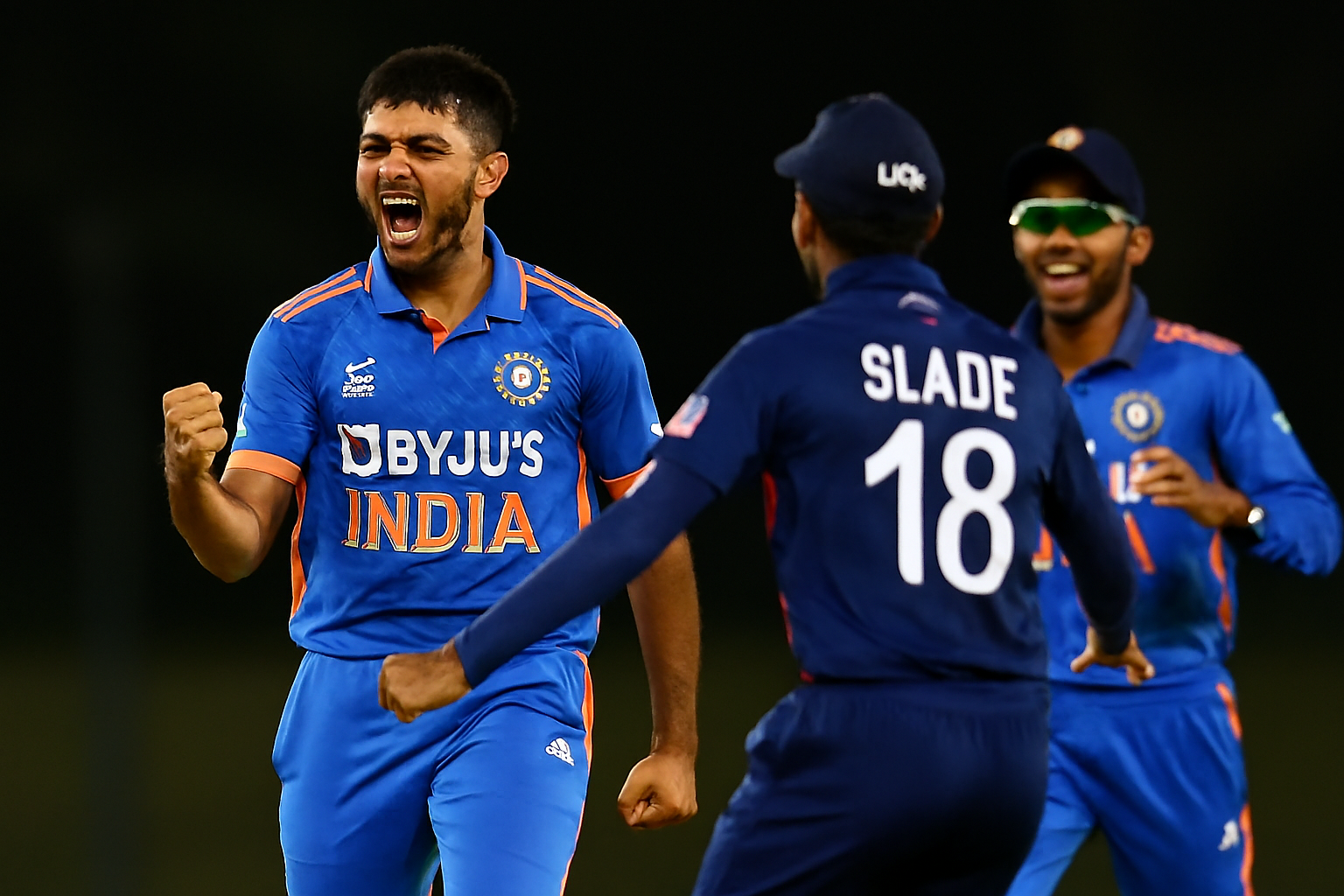 Henil Kundu celebrating after taking a wicket, with teammates rushing to congratulate him under stadium lights.